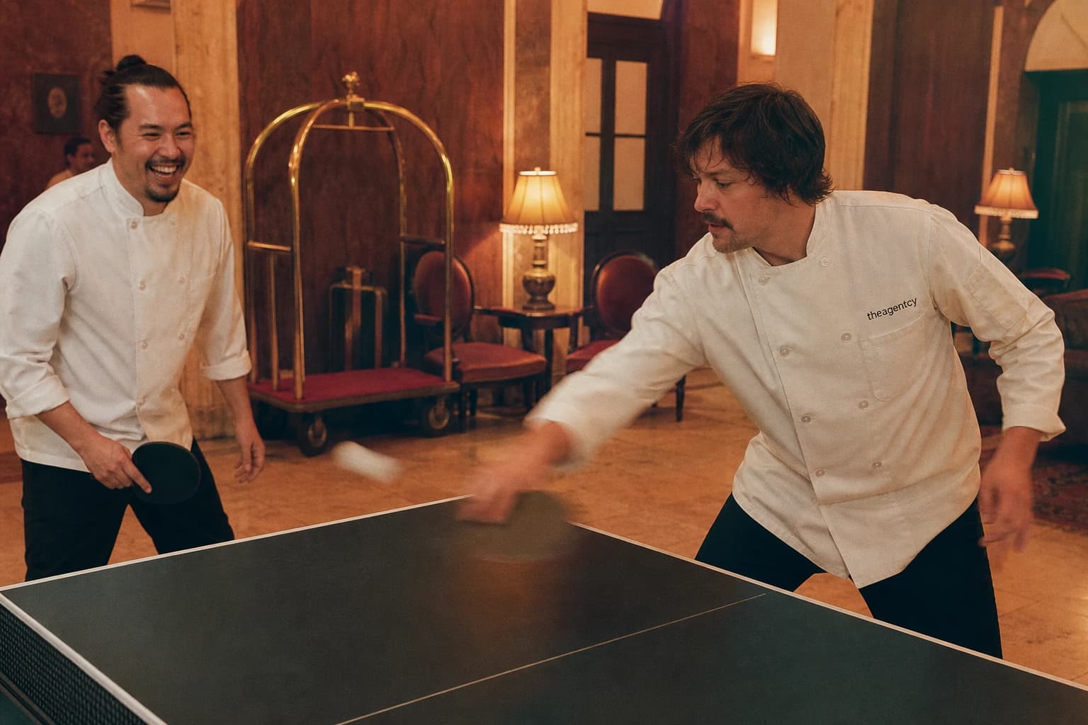 Dos cocineros jugando al ping pong en el lobby de un hotel.